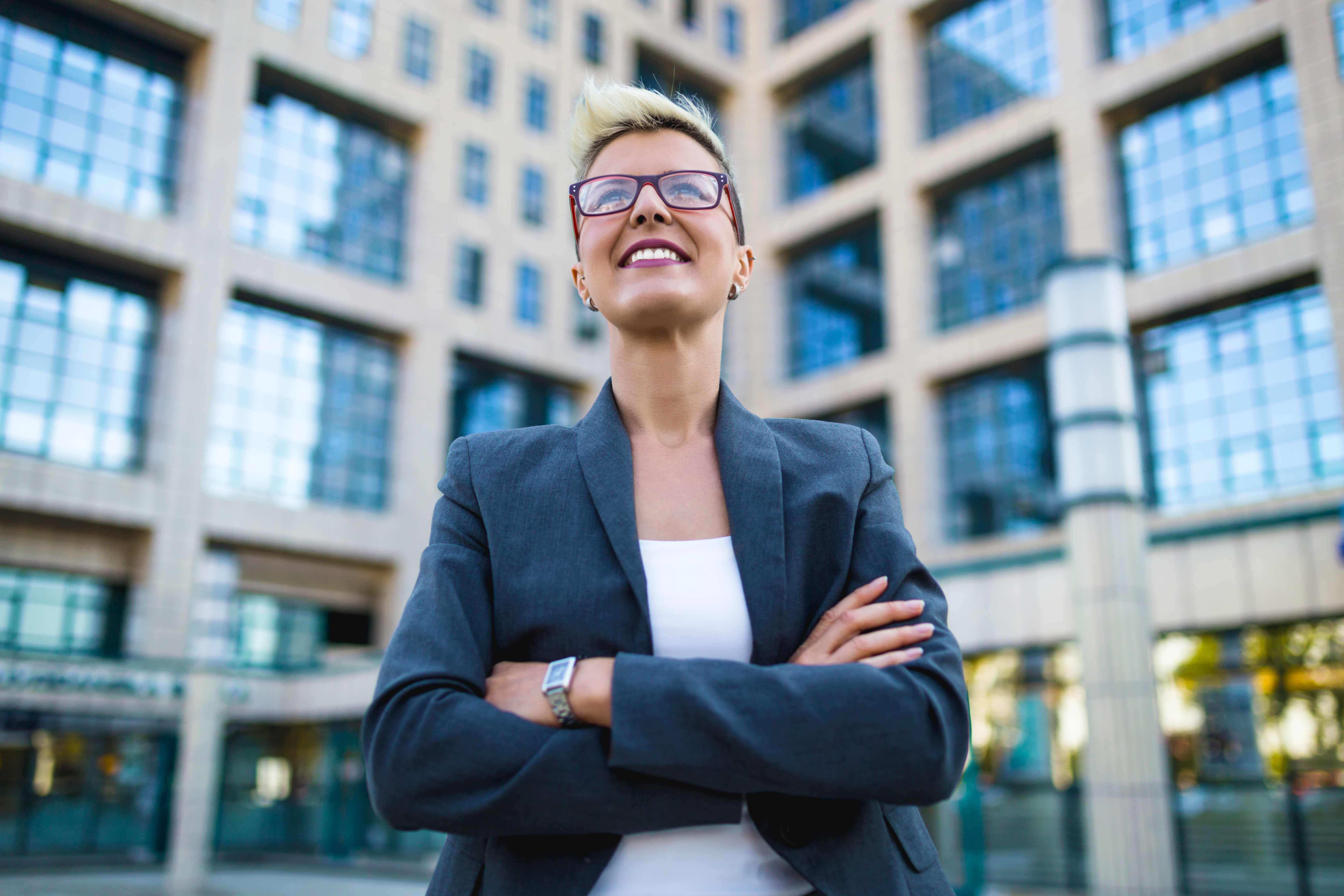 A smiling woman in business wear standing in front of an urban building.